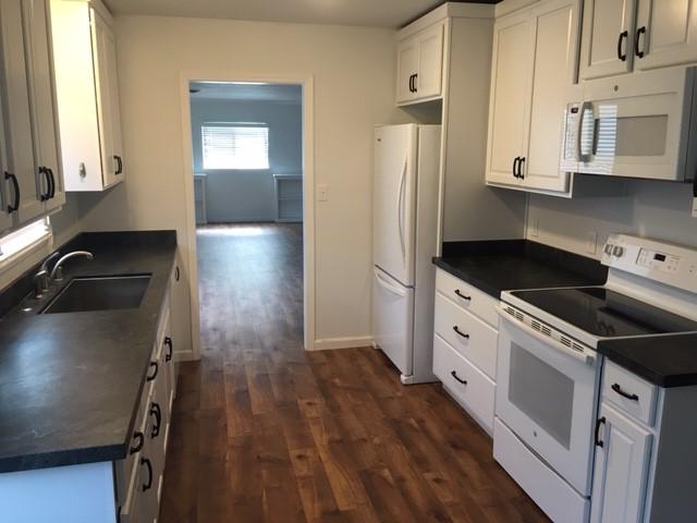 Galley-style kitchen with white cabinets and wood floors